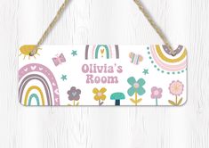 a wooden sign hanging from a rope on top of a white wood wall with flowers and rainbows