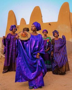 a group of women standing next to each other in front of an adobe building with arches