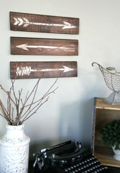 an old typewriter sits next to two wooden signs with arrows on them, and a white vase filled with twigs