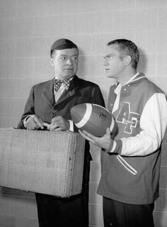 two men standing next to each other holding a suitcase and football ball in their hands