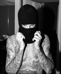 a man with tattoos and a black mask covering his face is standing in front of a mirror