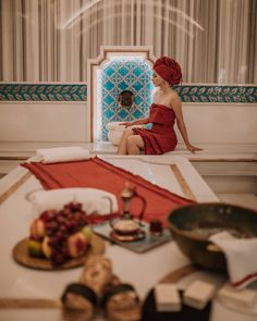 a woman in a red dress sitting on a table with food and drinks around her