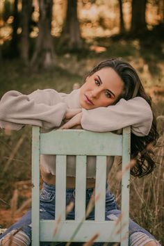 a woman is sitting on a chair in the woods with her arms folded over her head