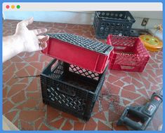 a hand reaching for a red and black plastic box on top of some other boxes