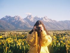 a woman in a yellow jacket taking a photo with her camera on a field of wildflowers