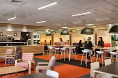 people are sitting at tables and chairs in an open area with orange carpeted flooring