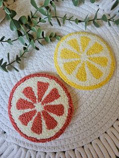 two crocheted fruit coasters sitting on top of a white table next to green leaves