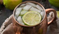 a copper mug filled with ice and limes on top of a cloth covered table