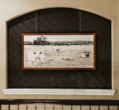 an old photo hangs on the wall above a fireplace mantel with cows in a field