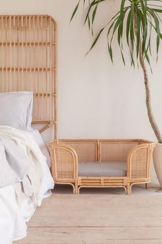 a bed with white sheets and pillows next to a plant in a pot on the floor