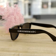 a pair of black sunglasses sitting on top of a wooden table next to pink flowers