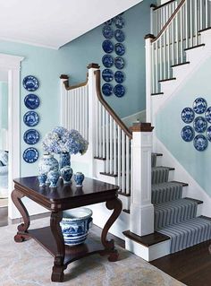 blue and white plates are on the wall next to a table with vases in it