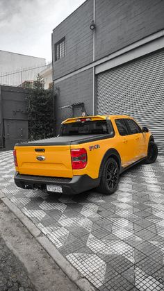 a yellow truck parked in front of a garage door on a brick road next to a building