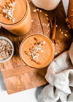 two glasses of carrot smoothie on a cutting board with cinnamons and other ingredients