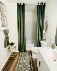 a white bathroom with green curtains and rugs on the floor, along with a toilet