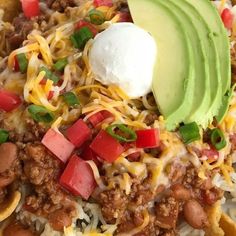 a white plate topped with nachos covered in cheese and toppings next to an avocado