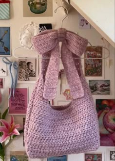 a crocheted purse hanging on a wall with pictures and flowers in the background