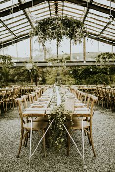 a long table set up with chairs and greenery in the center for an outdoor wedding reception