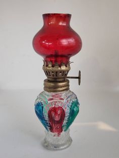 a red glass vase sitting on top of a white table next to a metal hook