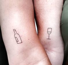 two people with matching tattoos on their arms holding wine glasses and a bottle in front of them