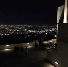 people standing on top of a building looking at the city lights in the night sky