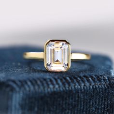 an emerald cut diamond sits on top of a blue velvet ring, which is gold