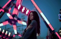 a woman standing in front of a carnival ride at night with her arms around her chest