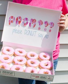 a person holding a box of donuts with pink frosting