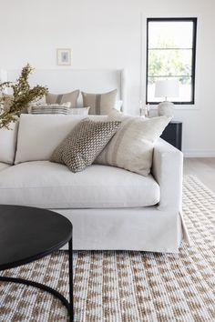 a living room with white couches and pillows on the back of it's sofa