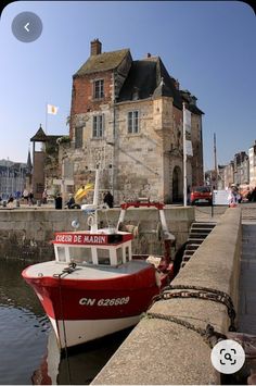 a red and white boat sitting in the water next to a stone wall with an old building on it