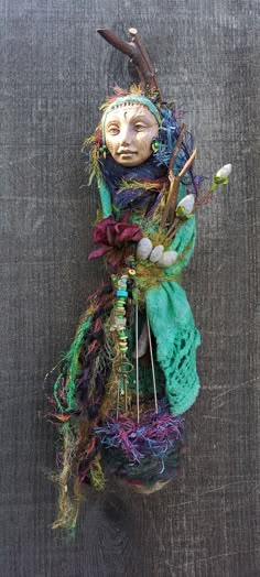 a doll made out of yarn with horns and feathers on it's head, sitting against a gray background