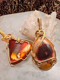 Celebrate the earthy beauty of mookaite jasper with these two unique handcrafted pendants, each wrapped in gold-tone copper wire. Choose from two captivating designs: a bold triangular pendant with striking patterns or an elegant oval pendant that highlights the stone's smooth, warm hues. The golden wire wrapping enhances the natural richness of the jasper, creating timeless pieces perfect for any occasion.     Mookaite jasper is a nurturing stone that is believed to promote vitality, courage, and a sense of adventure. Associated with the root, solar plexus, and sacral chakras, this stone supports grounding, stability, and emotional balance while inspiring confidence and a positive outlook. It is said to help with decision-making by encouraging flexibility and adaptability, making it an id Earthy Beauty, Embracing Change, Mookaite Jasper, Emotional Balance, Positive Outlook, Solar Plexus, Jasper Pendant, Oval Pendant, New Opportunities