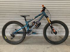 a blue mountain bike parked in front of a garage door with no wheels on it