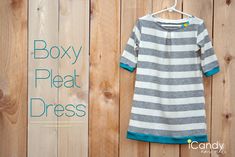 a dress hanging on a wooden wall with the words boxy pleat dress below it