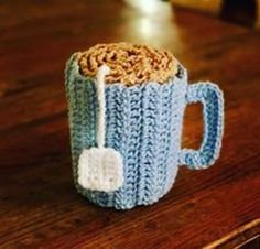 a crocheted coffee mug with a spoon in it sitting on a wooden table