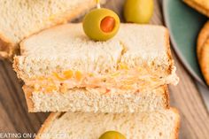 two sandwiches with olives on them are stacked next to crackers and an open - faced sandwich