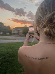 a woman with a tattoo on her back taking a selfie in front of the sunset