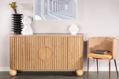 a wooden cabinet sitting in the corner of a room next to a chair and vase