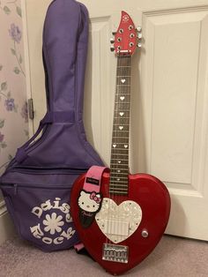 a red guitar with hello kitty on it next to a purple guitar case