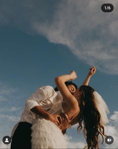 a bride and groom kissing under a cloudy blue sky