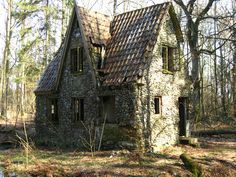 an old stone house in the woods with moss growing on it's roof and windows