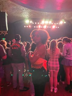 a woman standing in front of a crowd at a party with lights on the ceiling