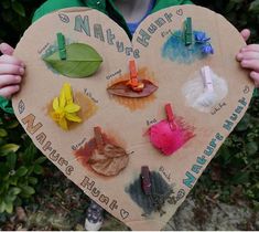 a person holding a heart shaped paper with different colored leaves on it and clips attached to them