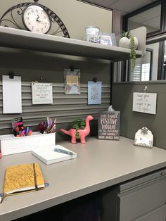 an office desk with several items on it and a large clock above the desk in the background