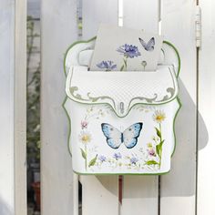 a butterfly painted purse hanging on the side of a white fence with flowers and butterflies