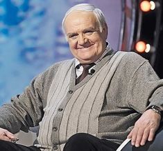 an older man sitting in a chair with his hands on his hips and smiling at the camera