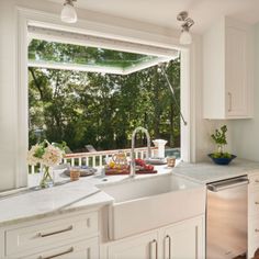 a kitchen with a sink, dishwasher and window looking out onto the trees