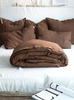 an unmade bed with brown pillows and blankets on it, next to a plant