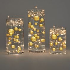 three glass vases filled with gold balls and lights on the inside one is empty