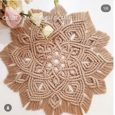 a close up of a doily on a white surface with flowers in the background